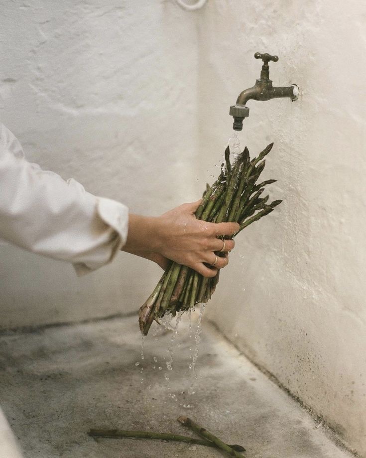 Hand wäscht grünen Spargel unter einem alten Wasserhahn